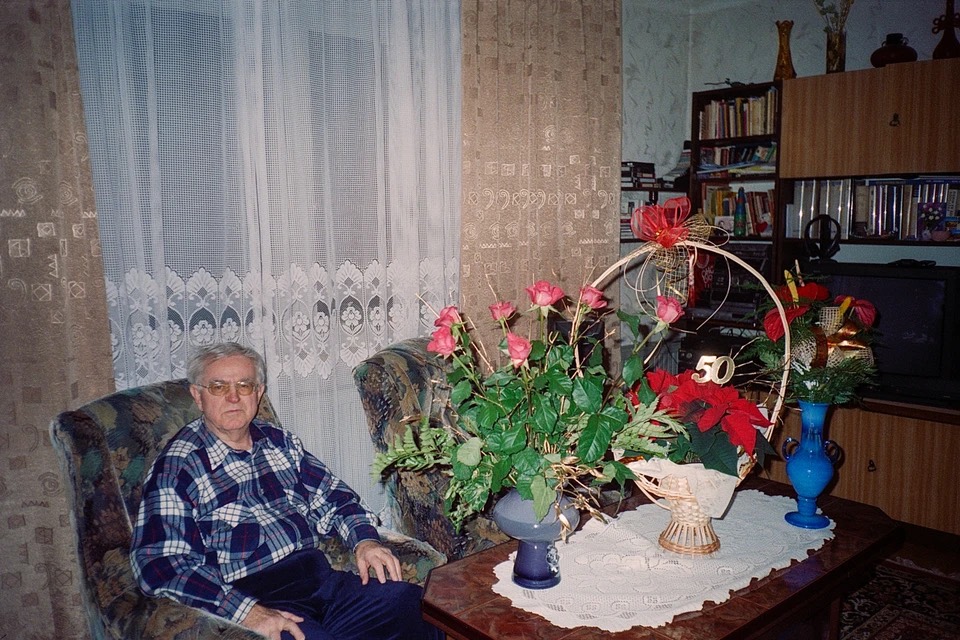 self-portrait of a man sitting in an armchair surrounded by bouquets of flowers